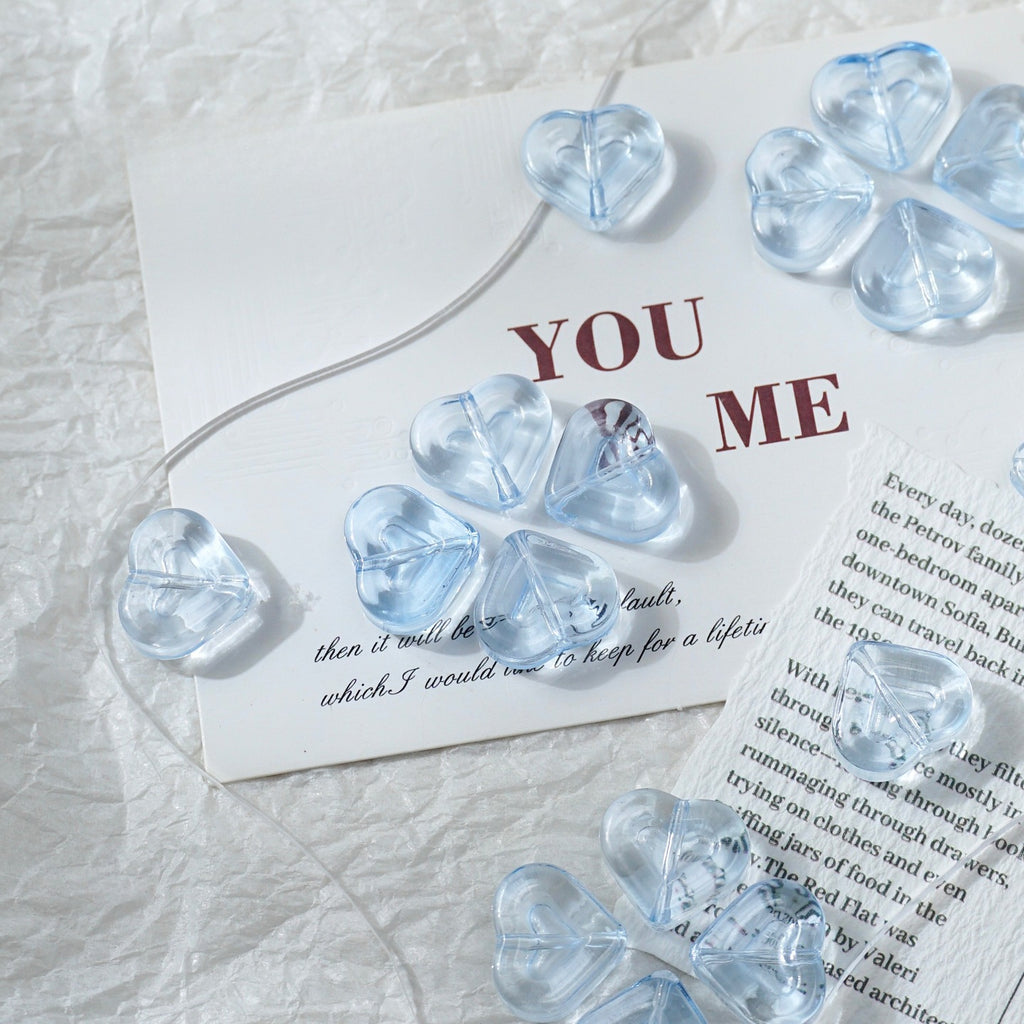 Clear heart-shaped glass beads on a cord, arranged on a white textured fabric with printed cards underneath.