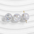 Three clear round resin beads filled with iridescent glitter flakes on a wavy white surface