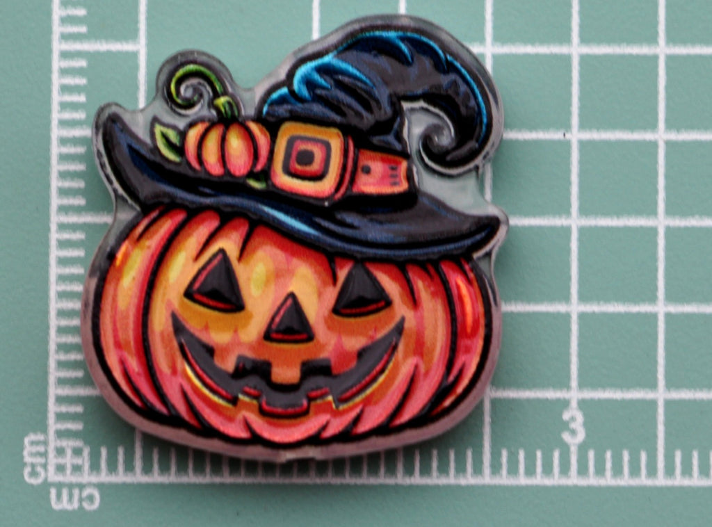 Halloween acrylic charm: carved orange pumpkin wearing black witch hat with pumpkin and buckle accents, on green cutting mat