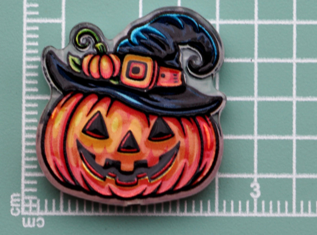 Halloween acrylic charm: carved orange pumpkin wearing black witch hat with pumpkin and buckle accents, on green cutting mat