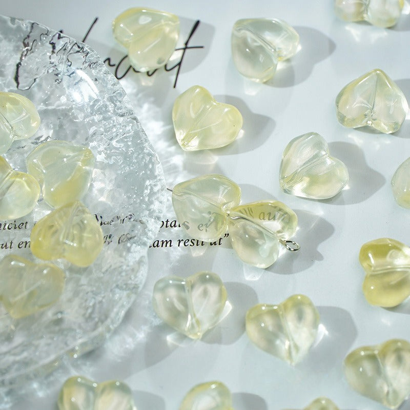 Pale yellow translucent heart-shaped glass beads scattered on a white surface
