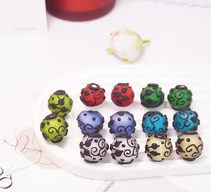 Colorful round frosted glass beads with black swirl patterns arranged on a white plate