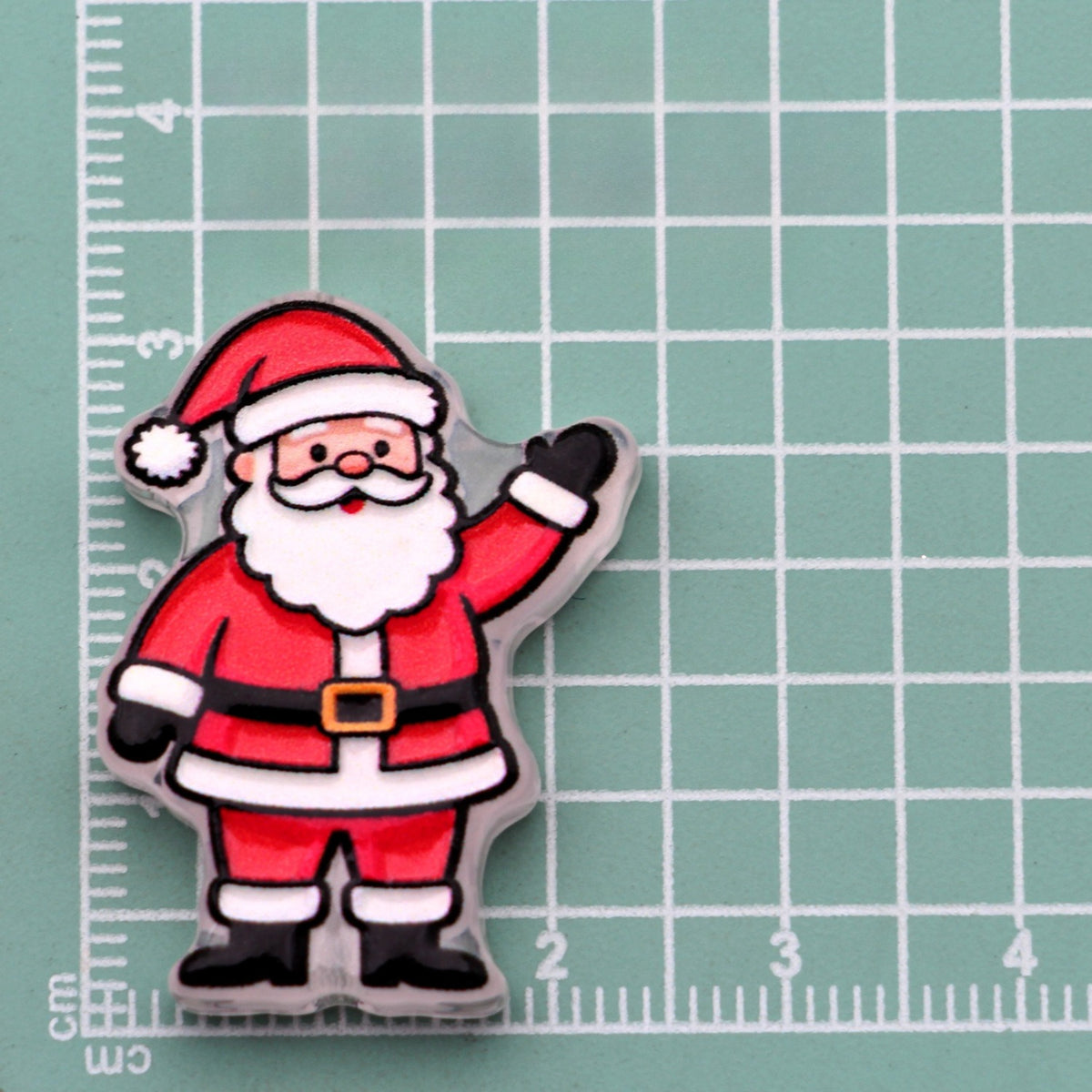 Waving Santa Claus acrylic charm in red suit on green cutting mat