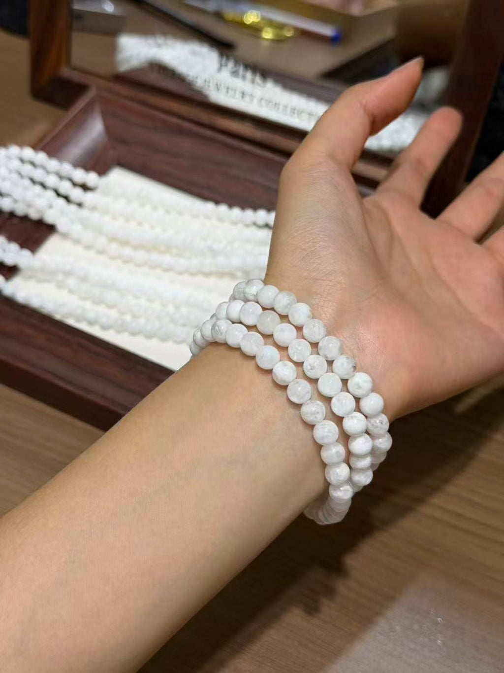 Close-up of a wrist wearing three strands of white round snowflake phantom quartz bead bracelets, display tray behind