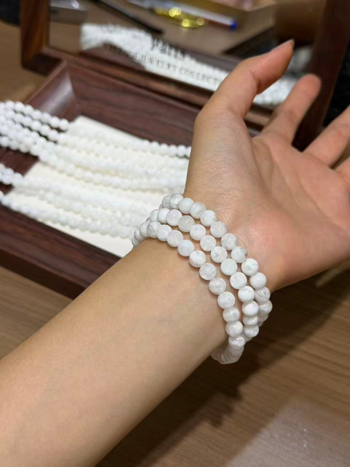 Close-up of a wrist wearing three strands of white round snowflake phantom quartz bead bracelets, display tray behind