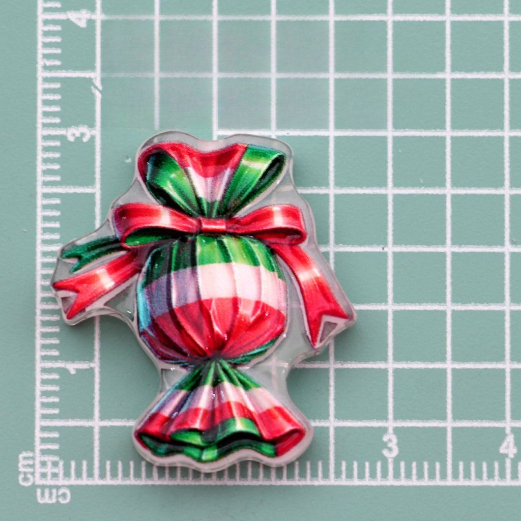 Wrapped candy acrylic charm with red, green and white stripes and bow on green cutting mat