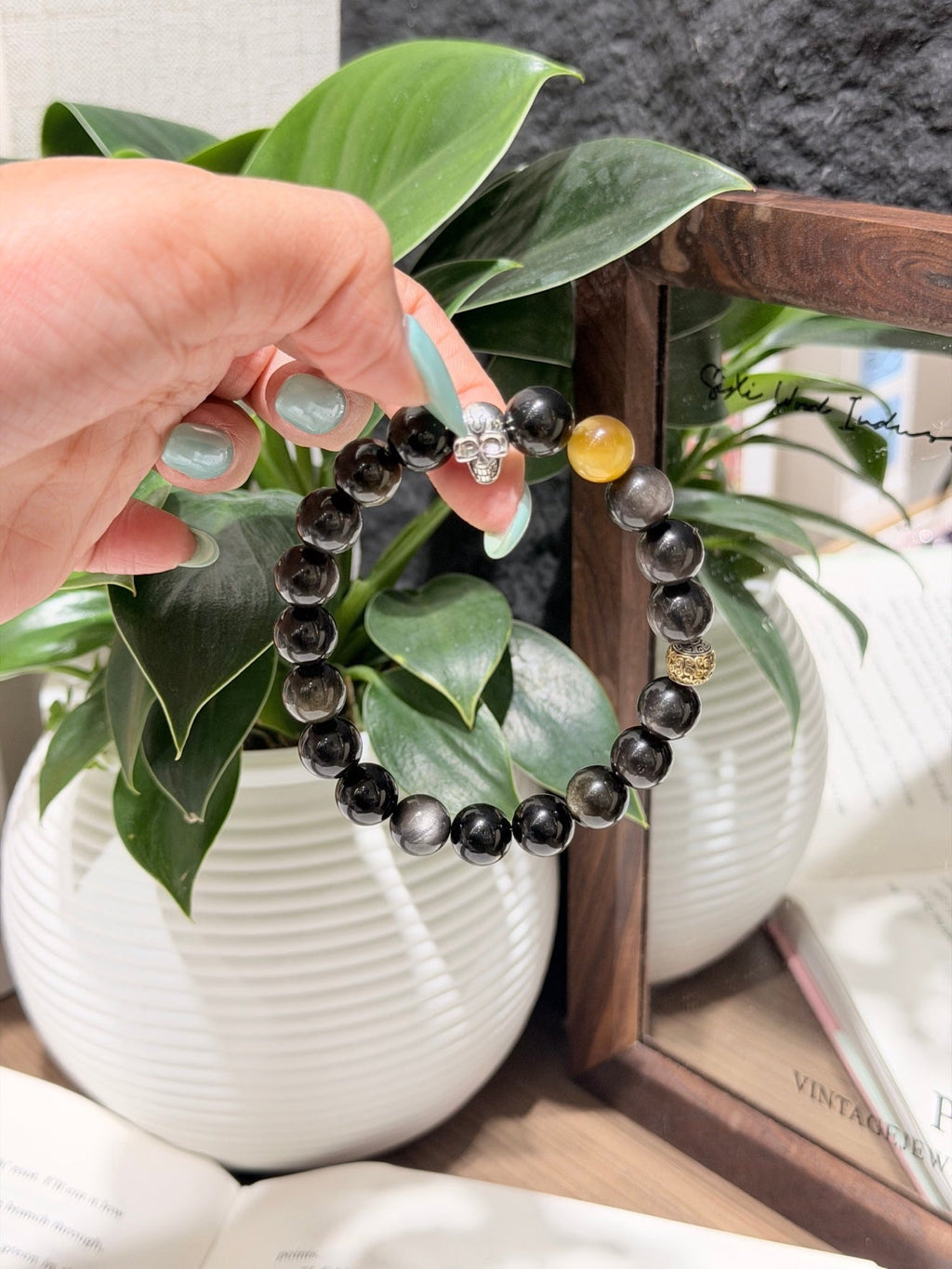 Hand holding dark gray beaded bracelet with silver charm and amber and gold accent beads