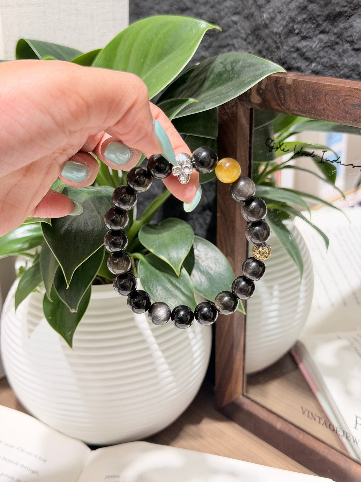 Hand holding dark gray beaded bracelet with silver charm and amber and gold accent beads