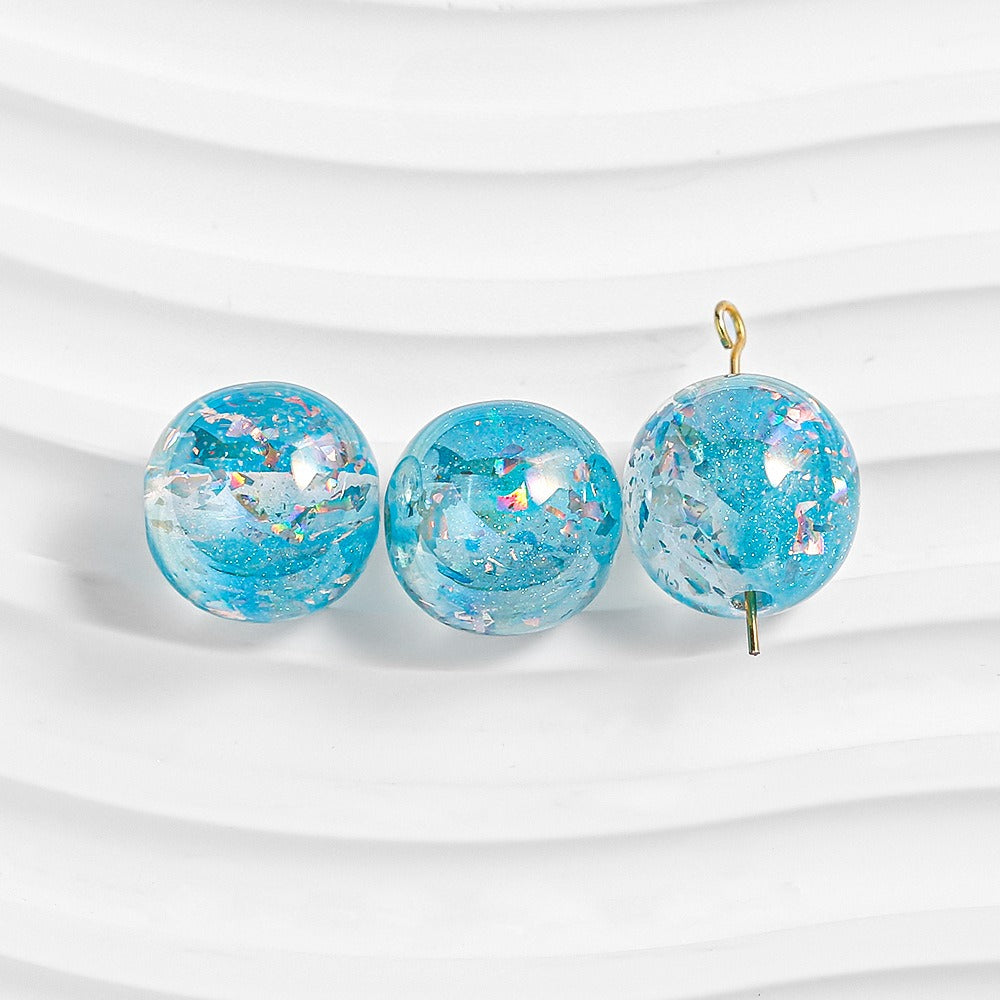 Three blue glitter resin beads on white; right bead has gold loop and pin