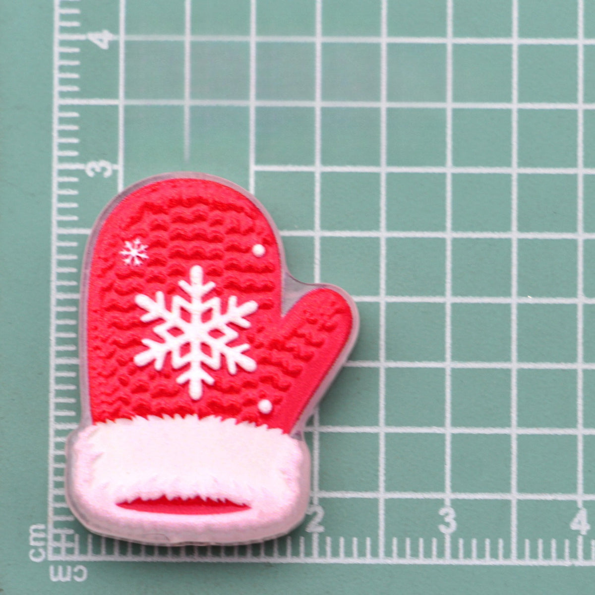 Red mitten acrylic charm with white snowflake and faux-fur trim on green cutting mat
