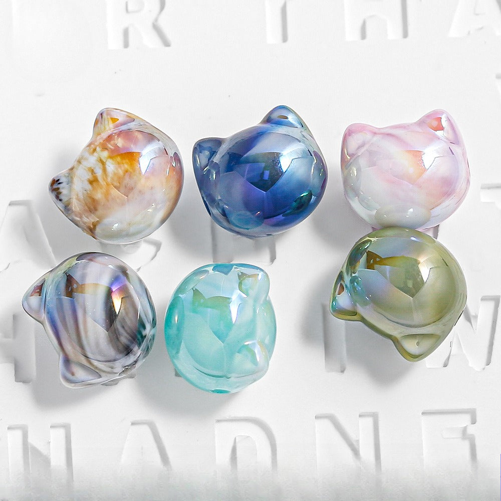 Six iridescent cat head focal beads in assorted colors on a white background.