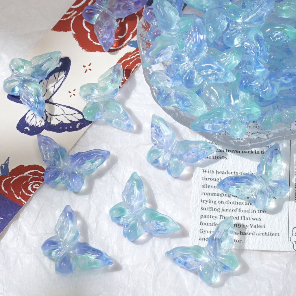 Light blue and aqua translucent butterfly-shaped beads scattered on a white textured surface