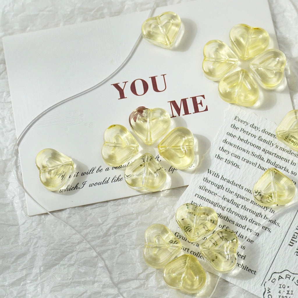 Heart-shaped translucent yellow glass beads with elastic cord on a white textured fabric with printed cards