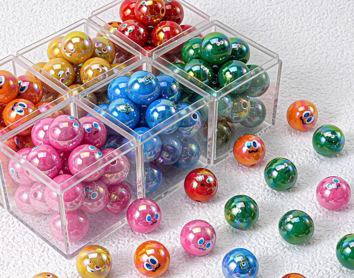 Colorful resin round beads with cartoon faces in clear compartment boxes, some scattered on white textured surface