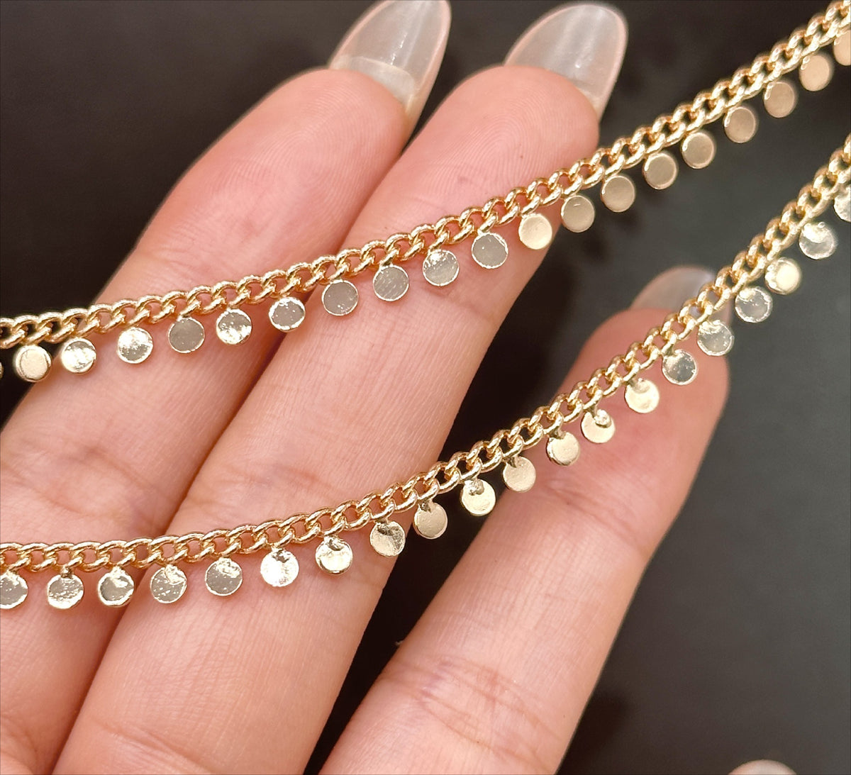 Close-up of a hand holding two delicate gold disc chains with small flat metallic disc charms.