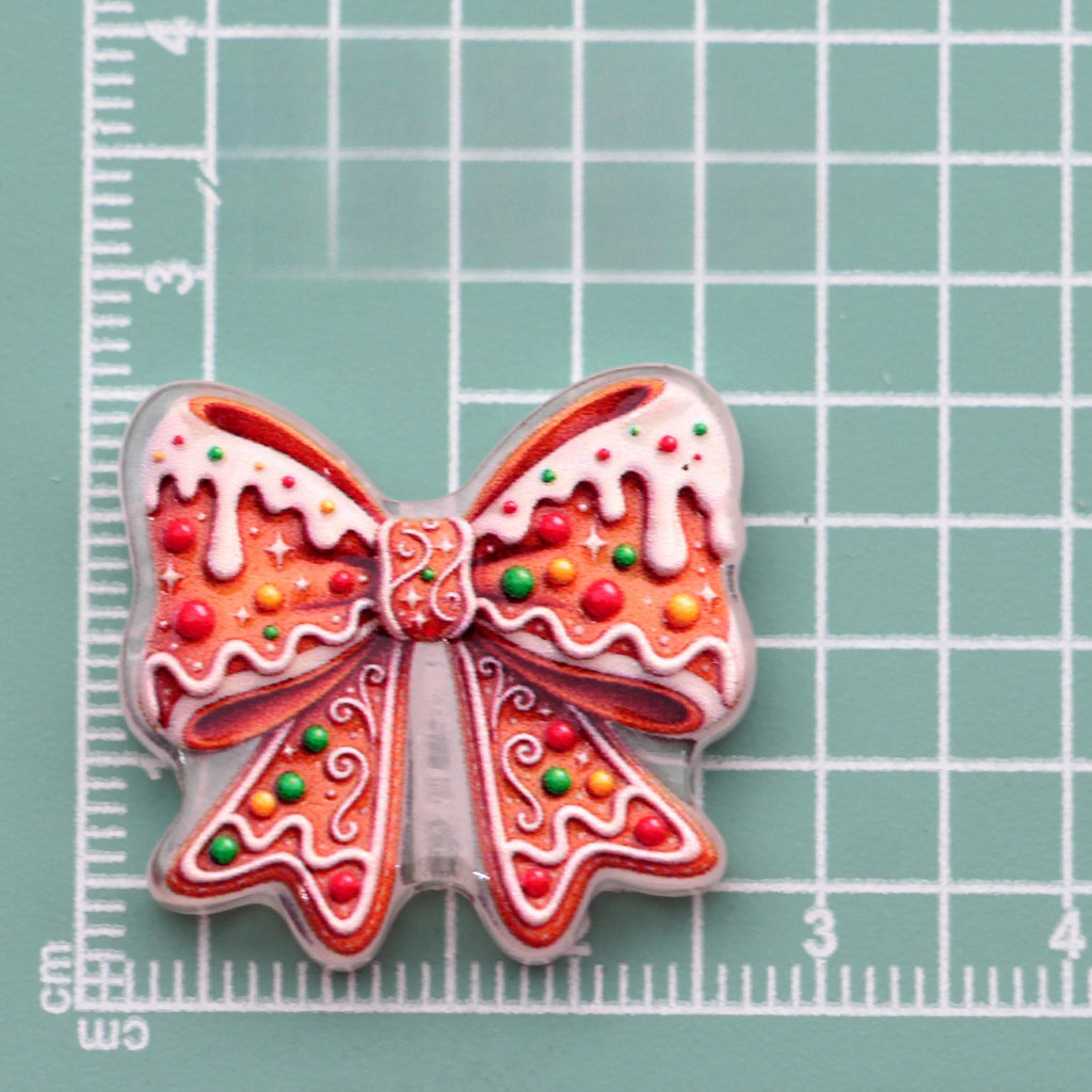Gingerbread bow acrylic charm with white icing and colorful sprinkles on green cutting mat
