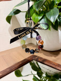 Multi-gemstone beaded car charm with black ribbon printed LOVE IS PERMANENT in gold lettering