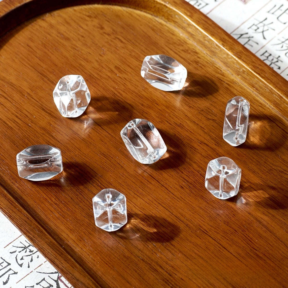 Six clear faceted glass beads on a polished wooden tray with printed paper in the background