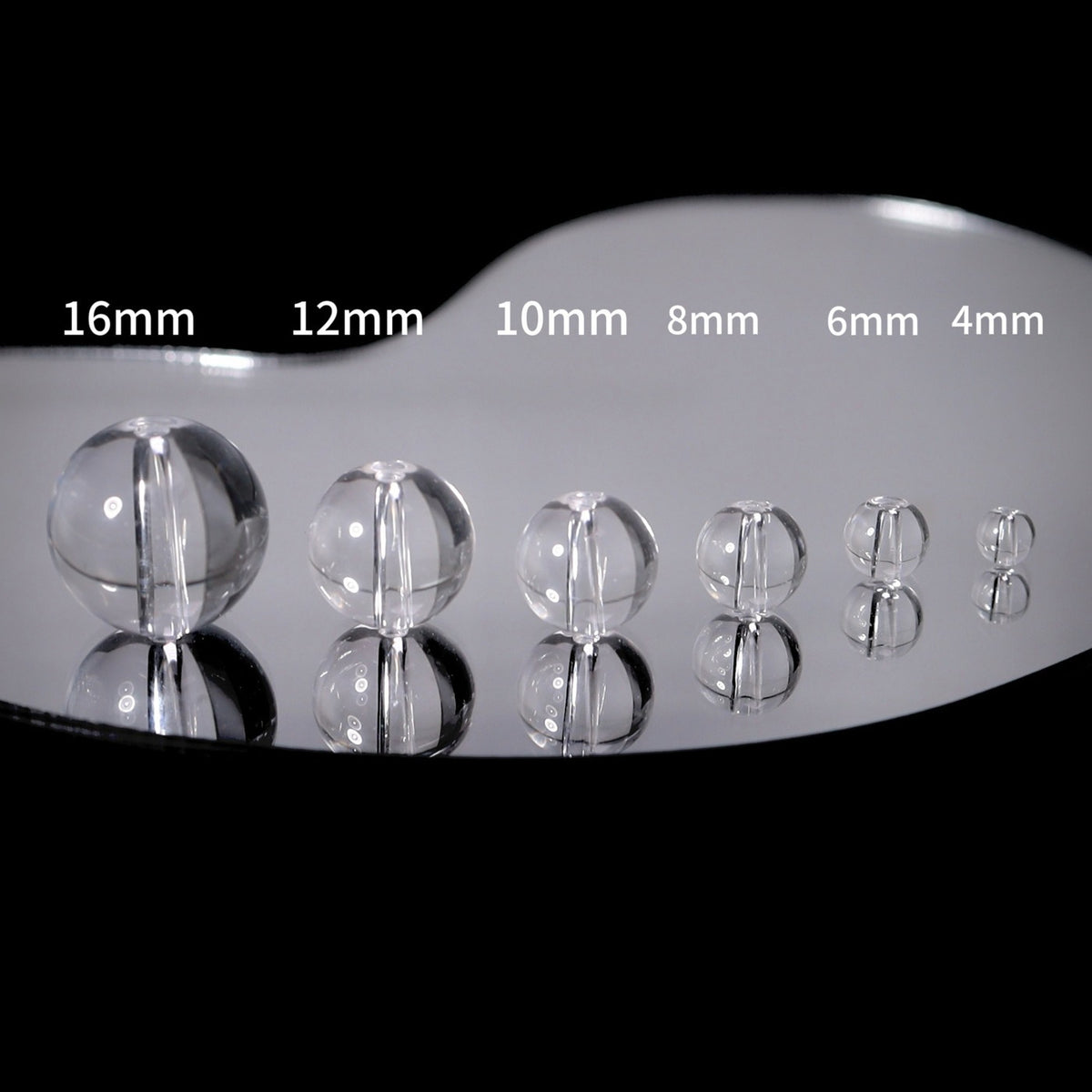 Six clear glass sphere beads in sizes 16mm to 4mm on black reflective surface
