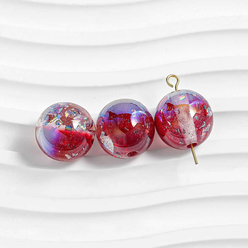 Three red-purple glitter resin beads on white; right bead has gold loop and pin