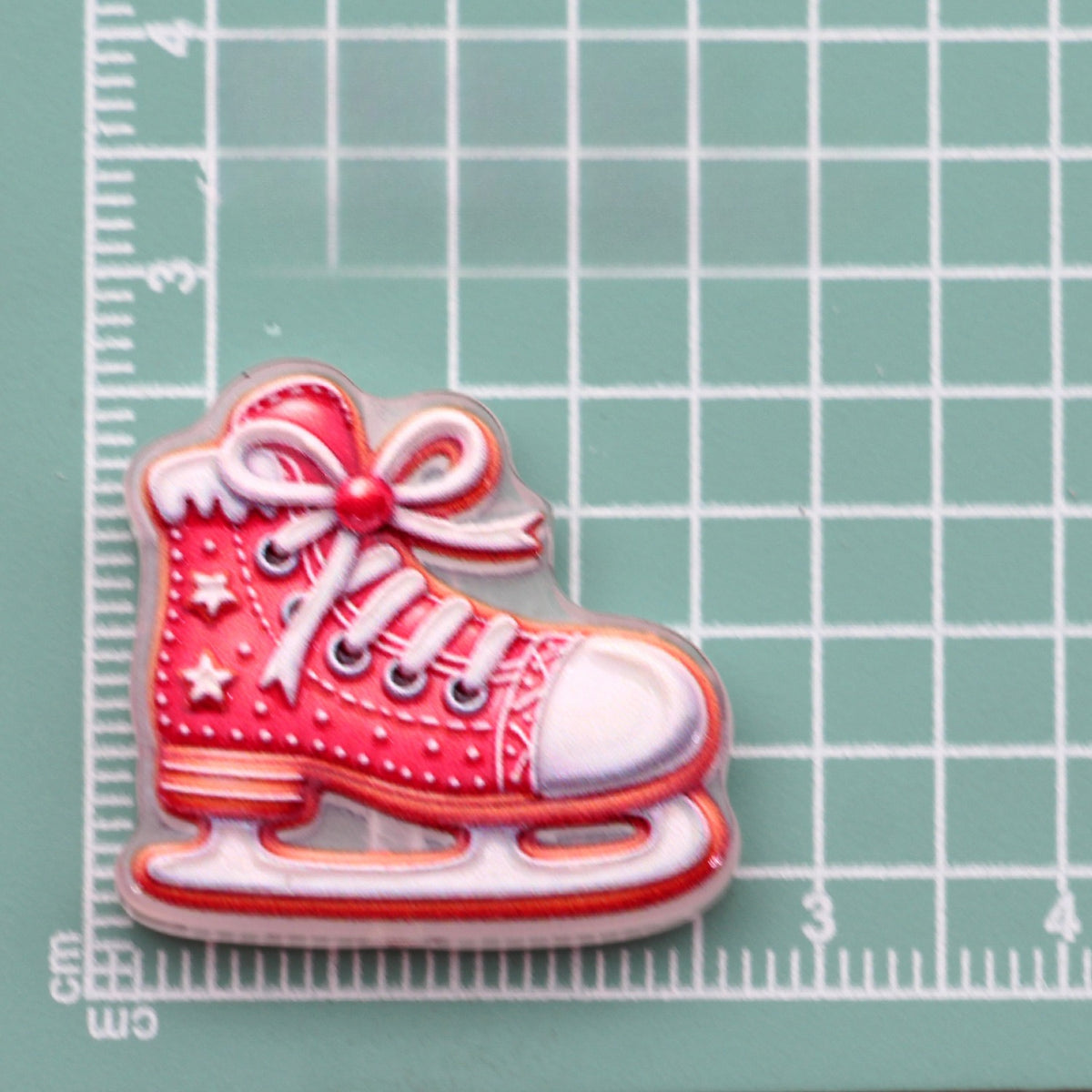 Red and white ice skate acrylic charm with bow and stars on green cutting mat