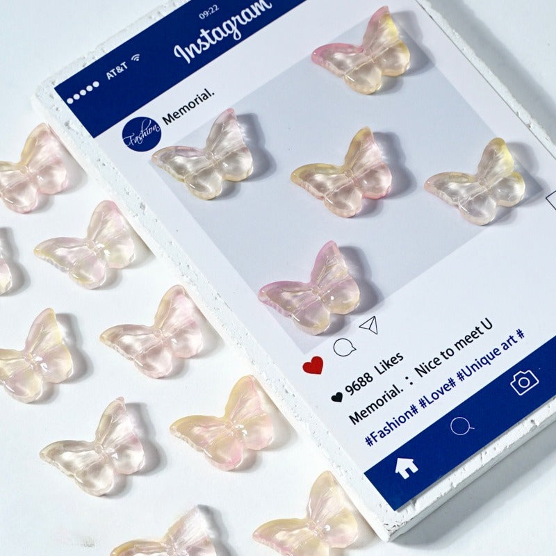 Translucent butterfly-shaped glass beads in pastel pink, peach, and pale yellow on white