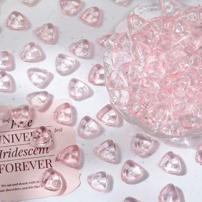 Pink iridescent triangular glass beads scattered on a white surface with a glass bowl