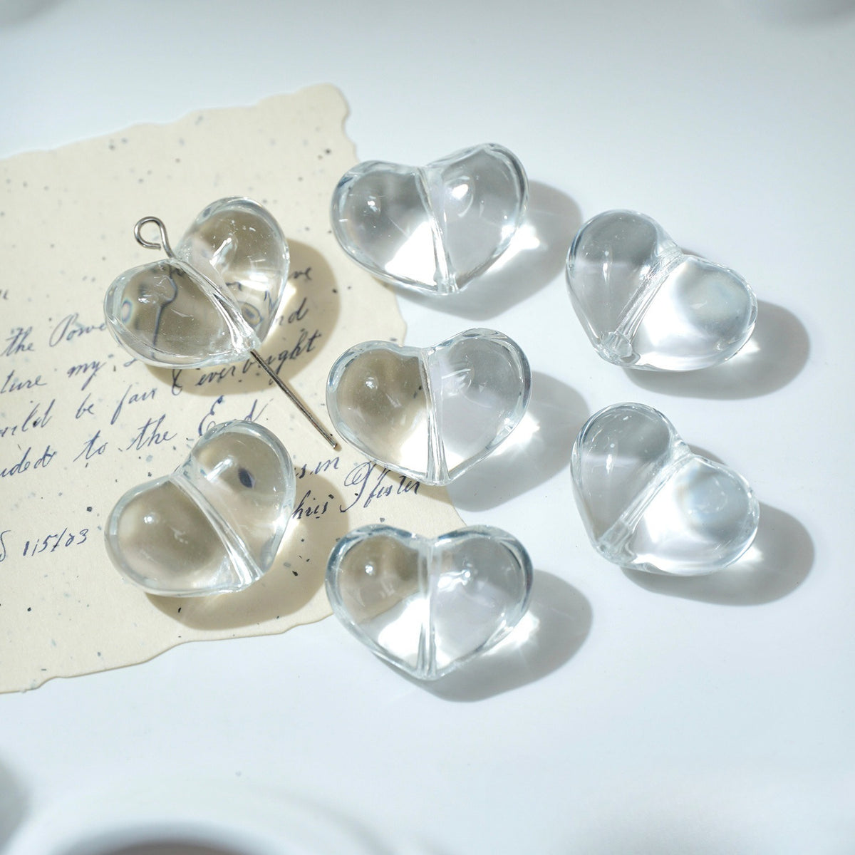 Six clear heart-shaped glass beads with silver split loops on white