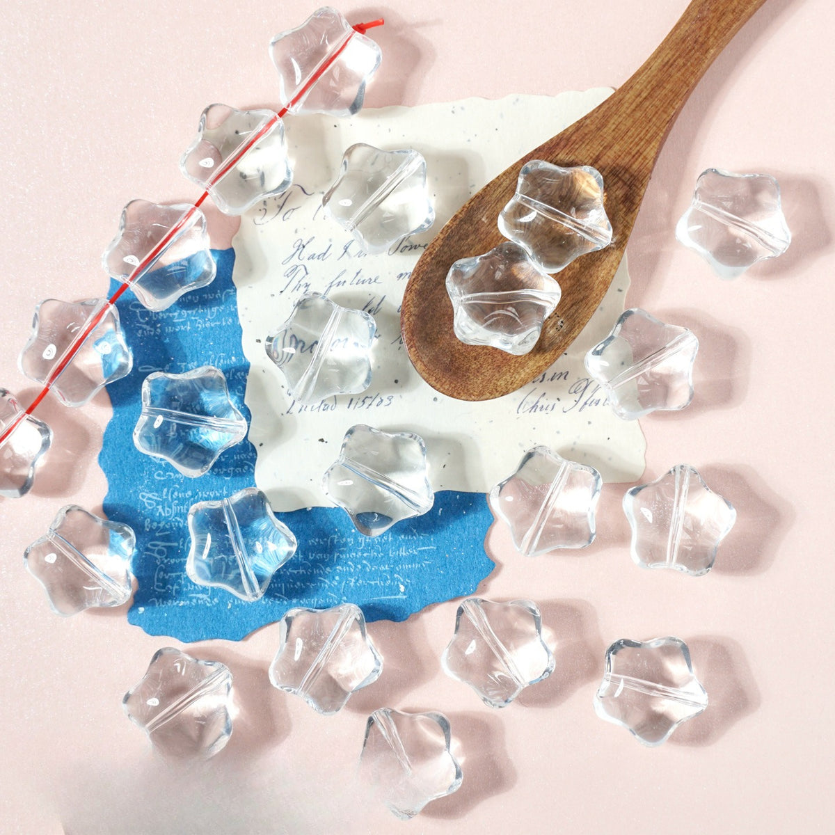 Clear star-shaped glass beads on light pink with a wooden spoon and blue paper note