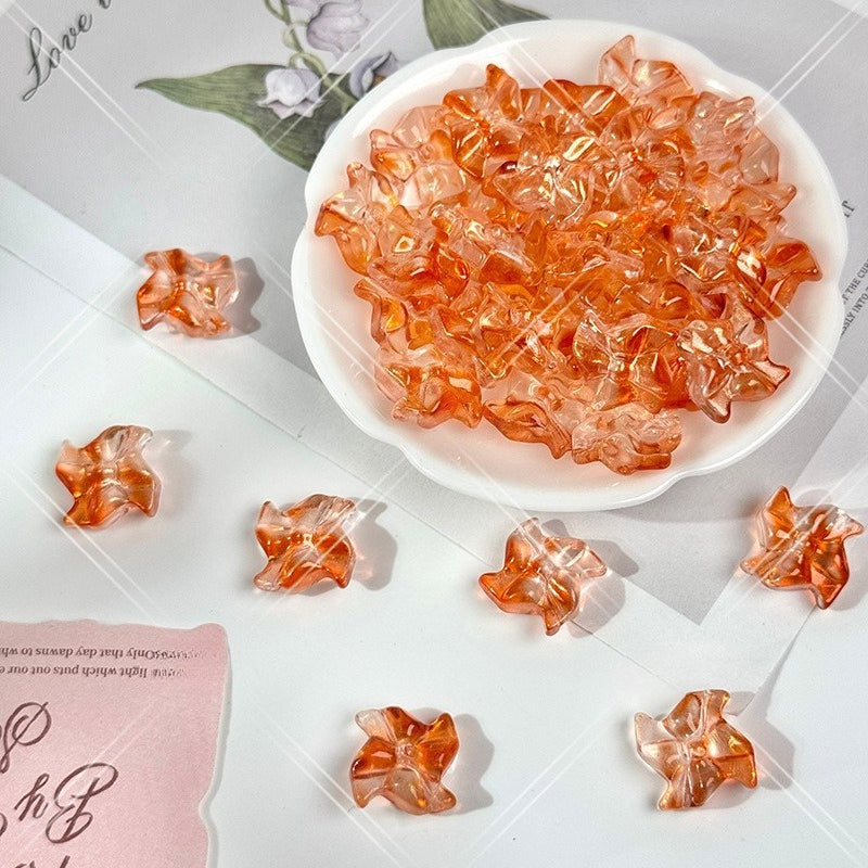 Clear amber-orange translucent 20mm carved glass windmill beads in a small white dish on a light surface