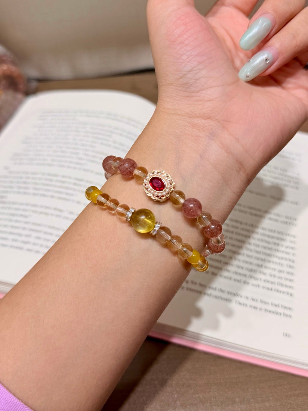 Two beaded bracelets with pink and yellow beads and a red gemstone medallion worn on a wrist over a book