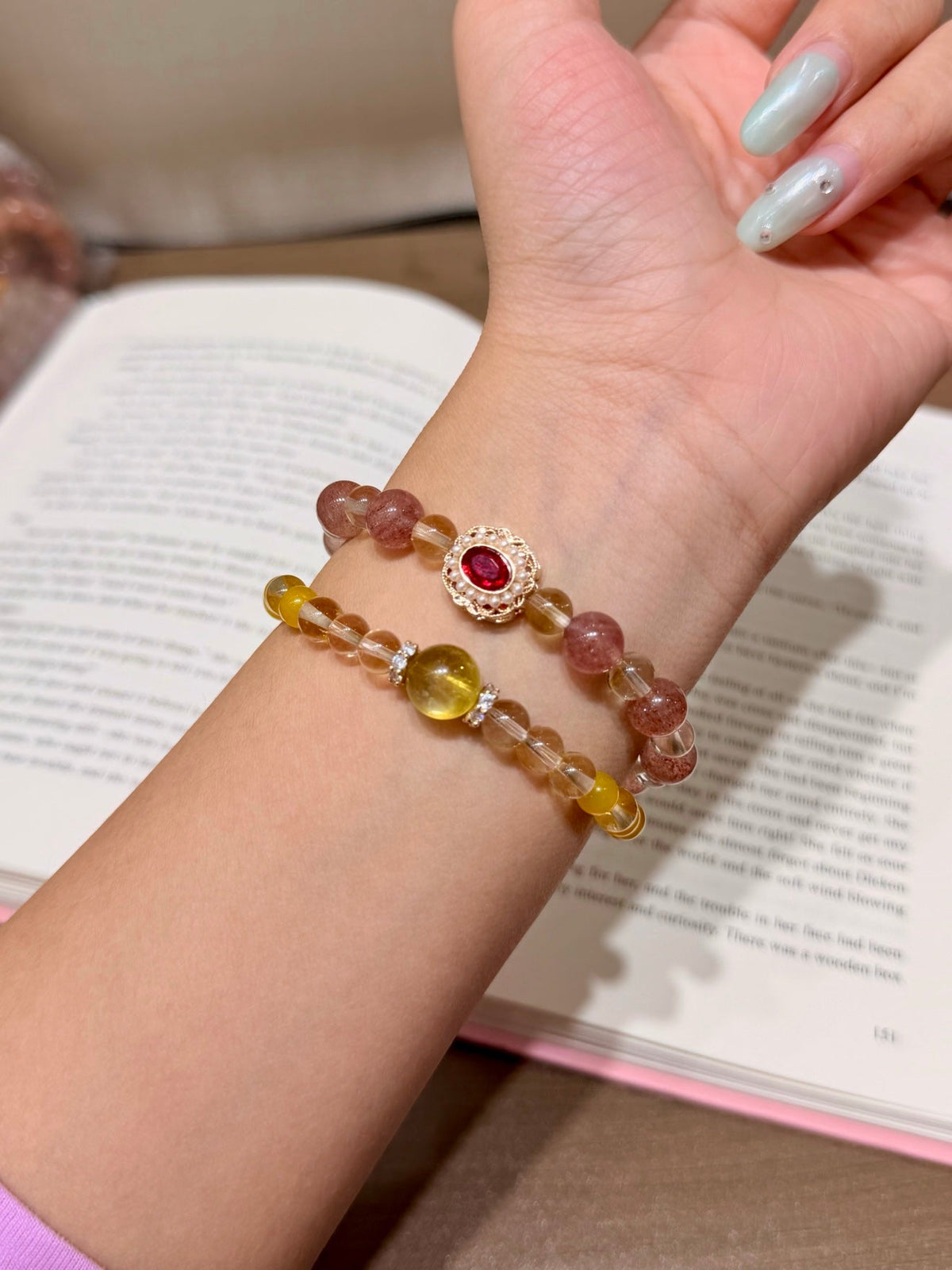 Two beaded bracelets with pink and yellow beads and a red gemstone medallion worn on a wrist over a book