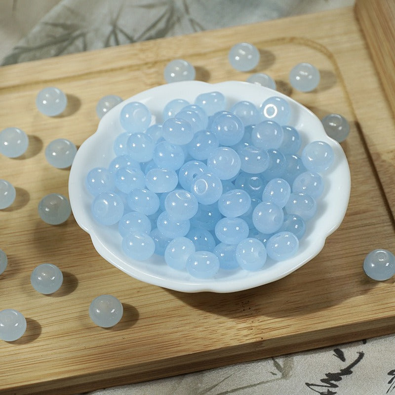 Light blue imitation jade glass beads in a scalloped bowl on a wooden board