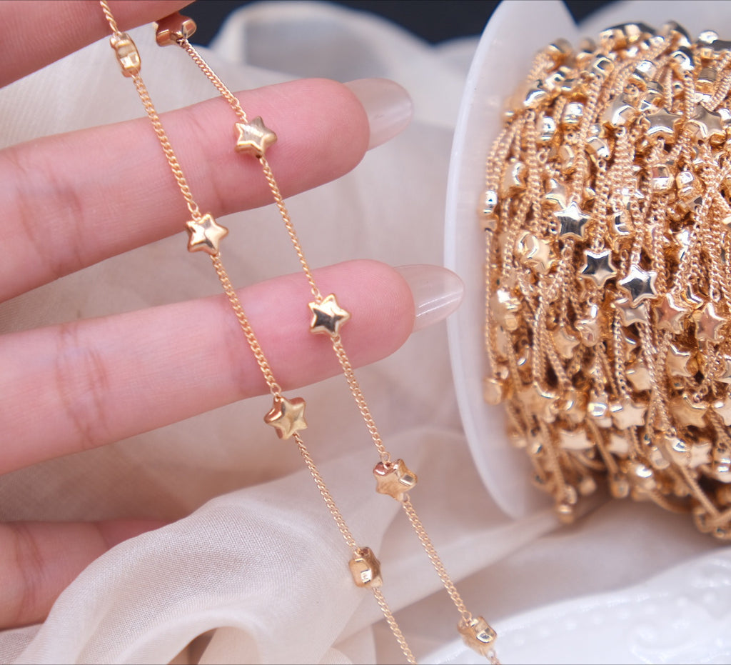 Close-up of fingers holding two rose gold star-bead chains beside a spool of chain