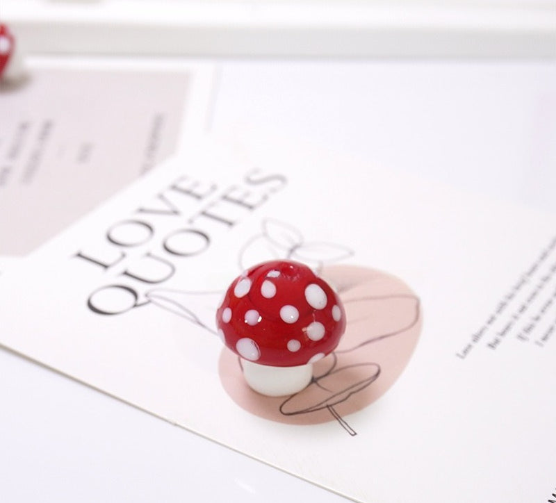 Glossy red mushroom-shaped glass bead with white spots on a 'LOVE QUOTES' card