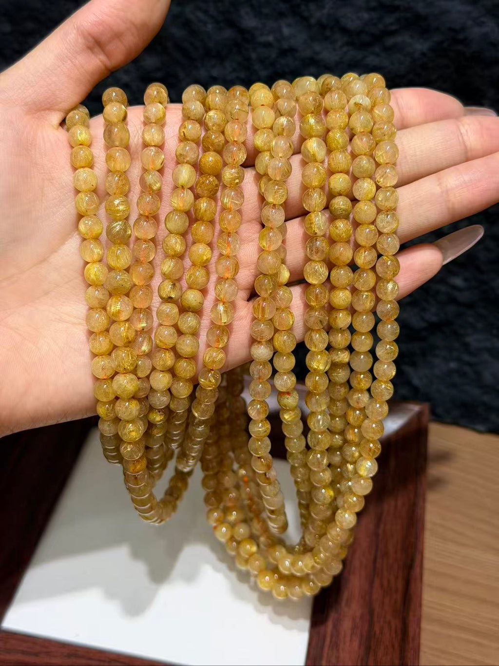 Hand holding multiple strands of golden rutilated quartz round beads