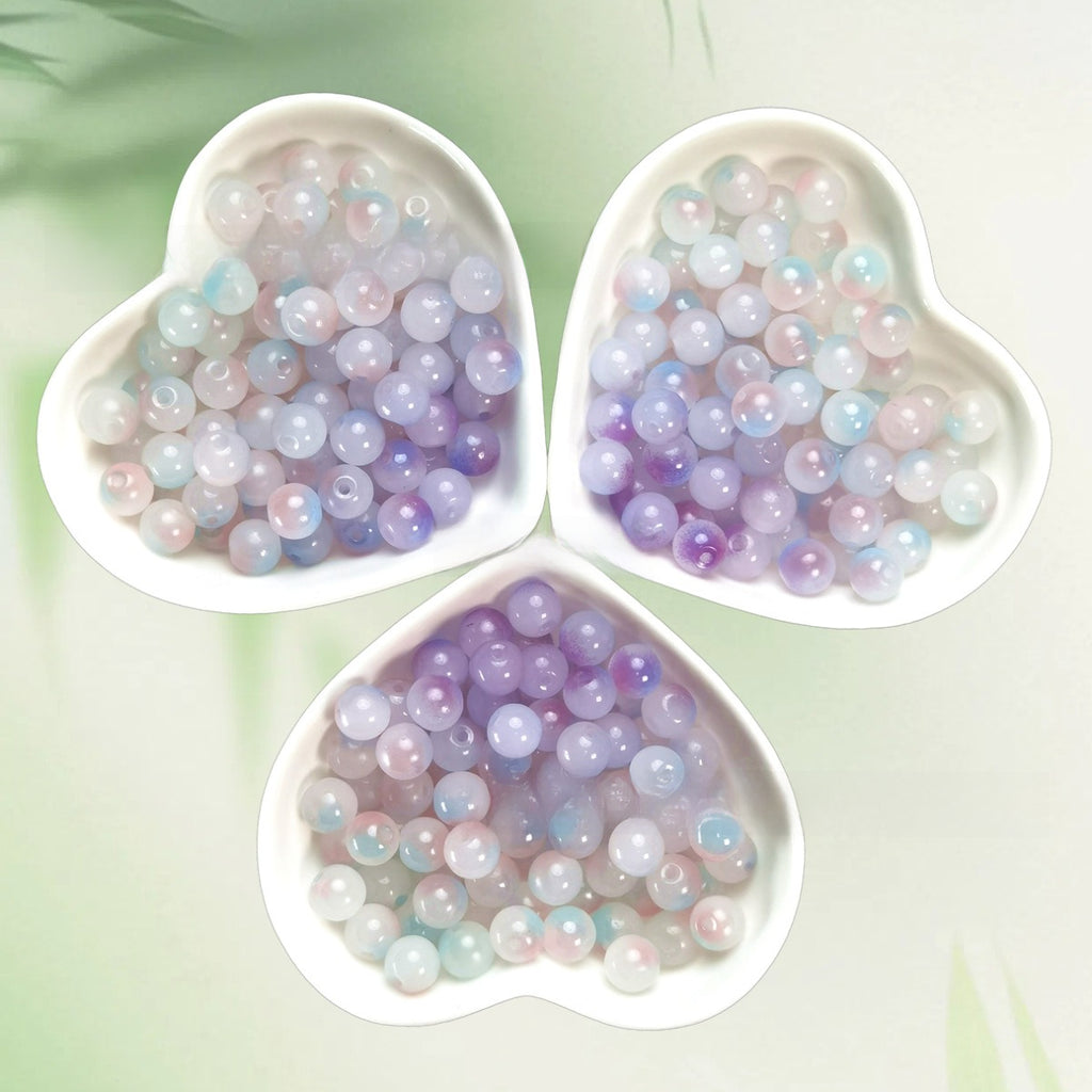 Three heart-shaped bowls of iridescent pastel lavender, pink, blue, and white beads