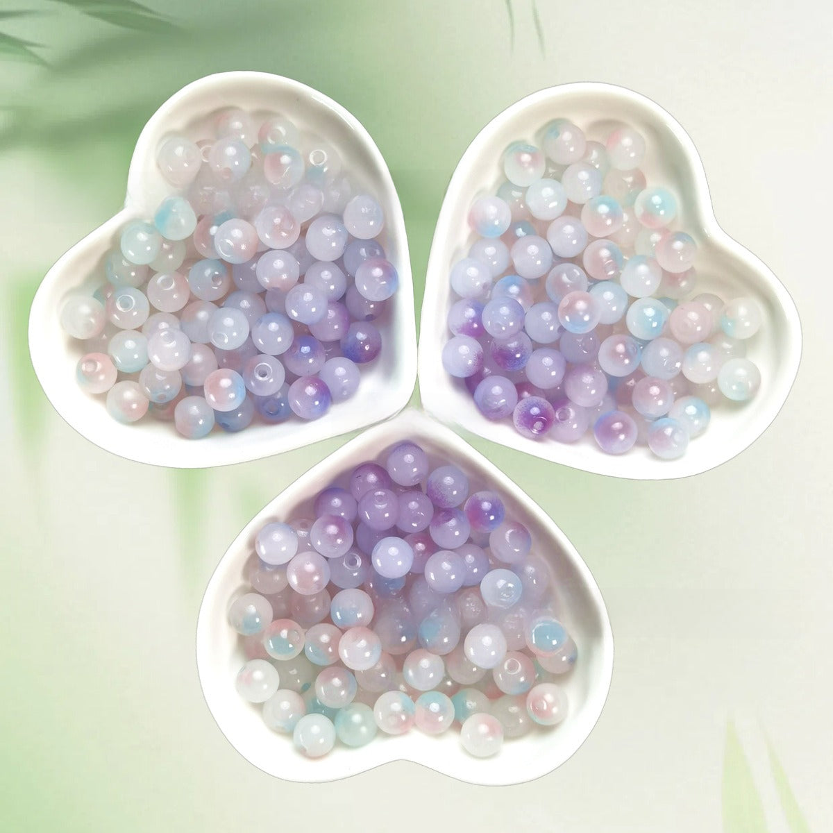 Three heart-shaped bowls of iridescent pastel lavender, pink, blue, and white beads