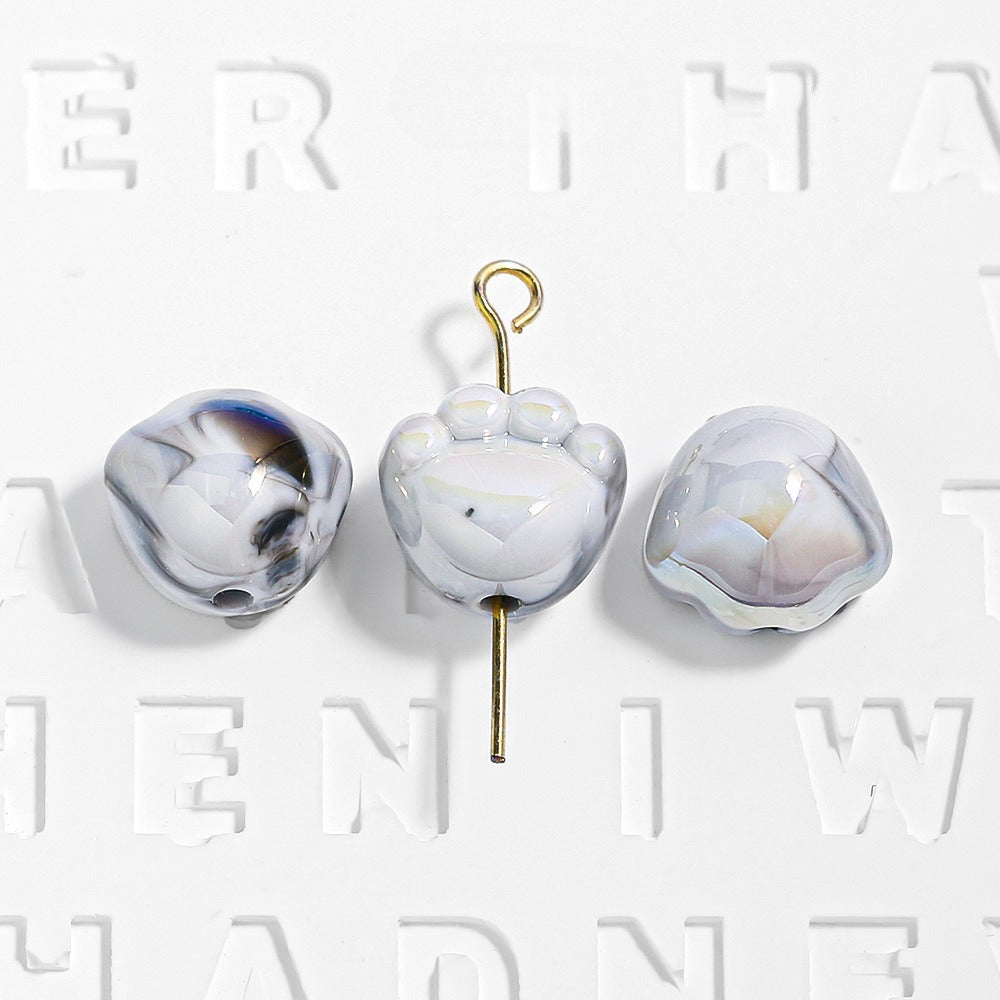 Three white marbled paw-shaped beads, one on a gold eye pin