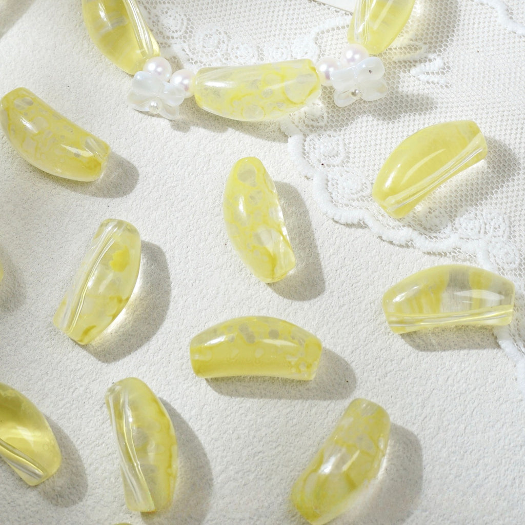 Translucent yellow marbled curved glass tube beads scattered on white textured fabric