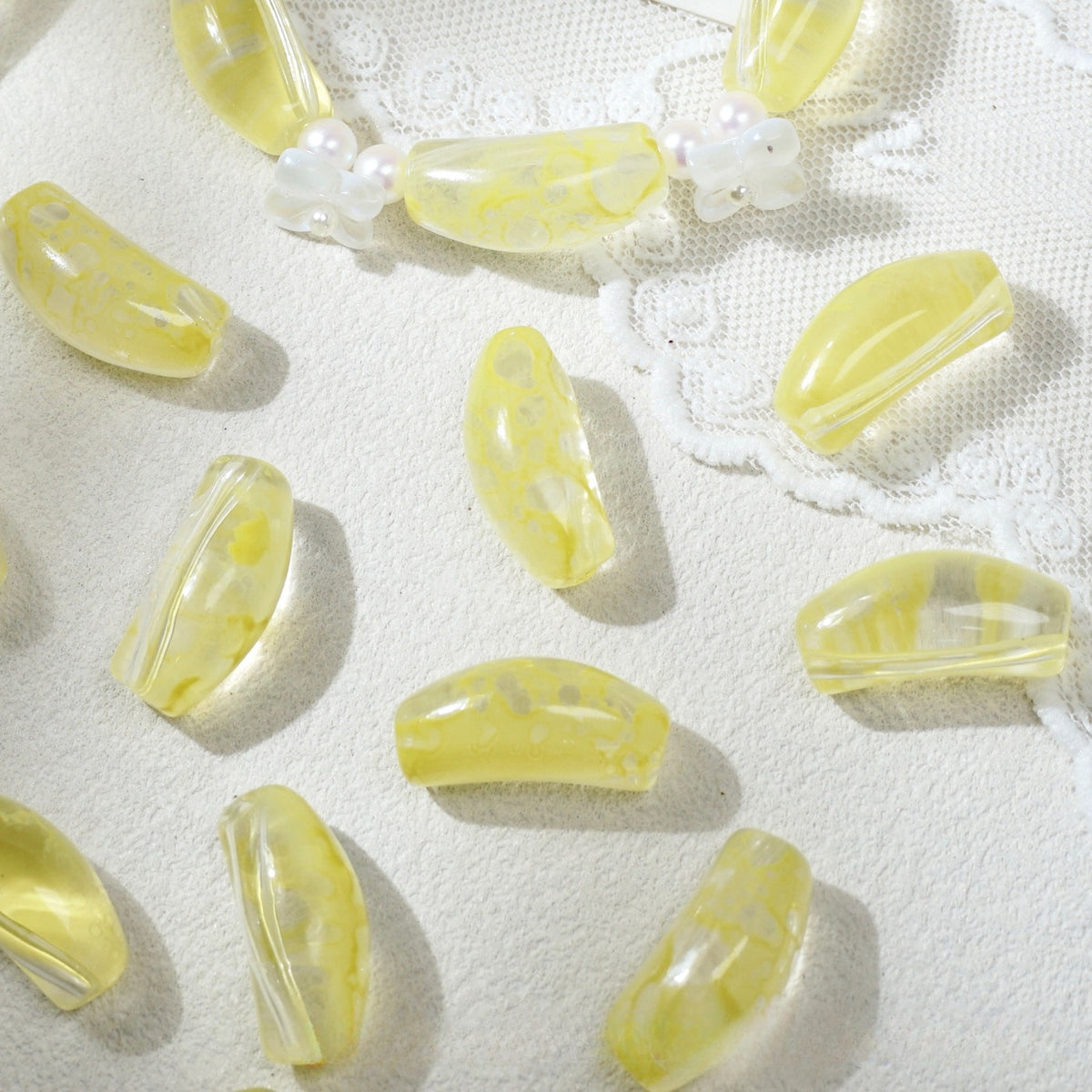 Translucent yellow marbled curved glass tube beads scattered on white textured fabric