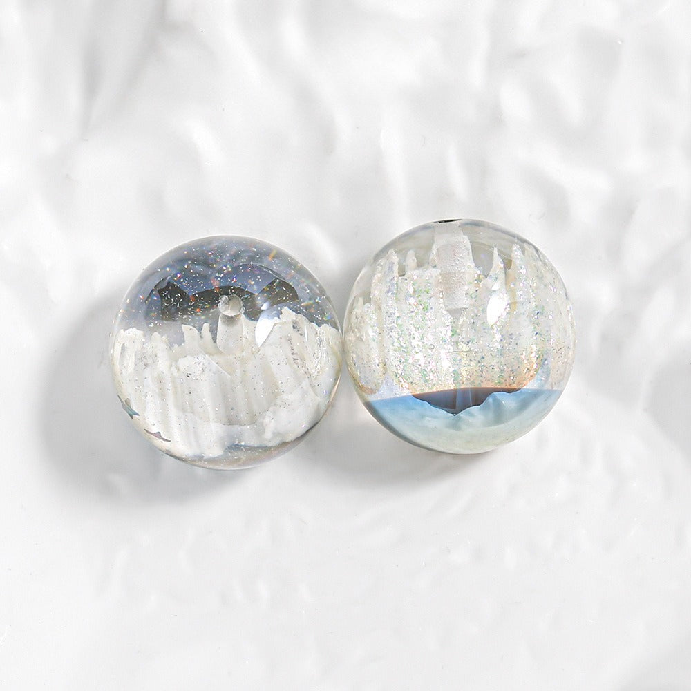 Two clear round resin beads with white castle scenes, silver glitter, and blue speckles on a textured white surface.
