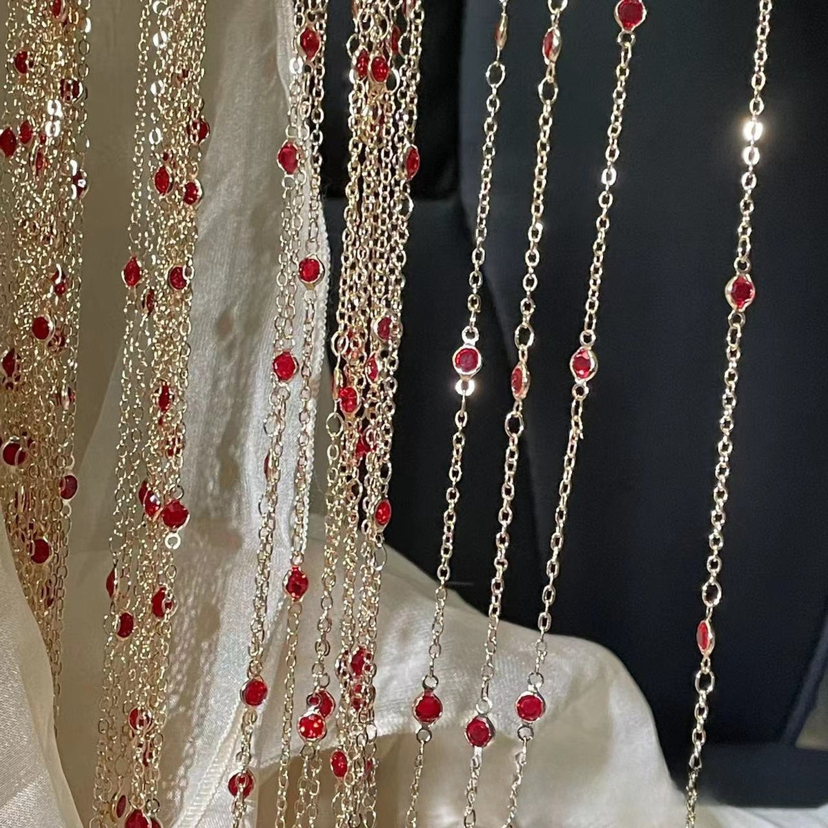 Gold chain curtains with red faceted beads hanging in vertical strands, shown against a dark background with a cream fabric drape.