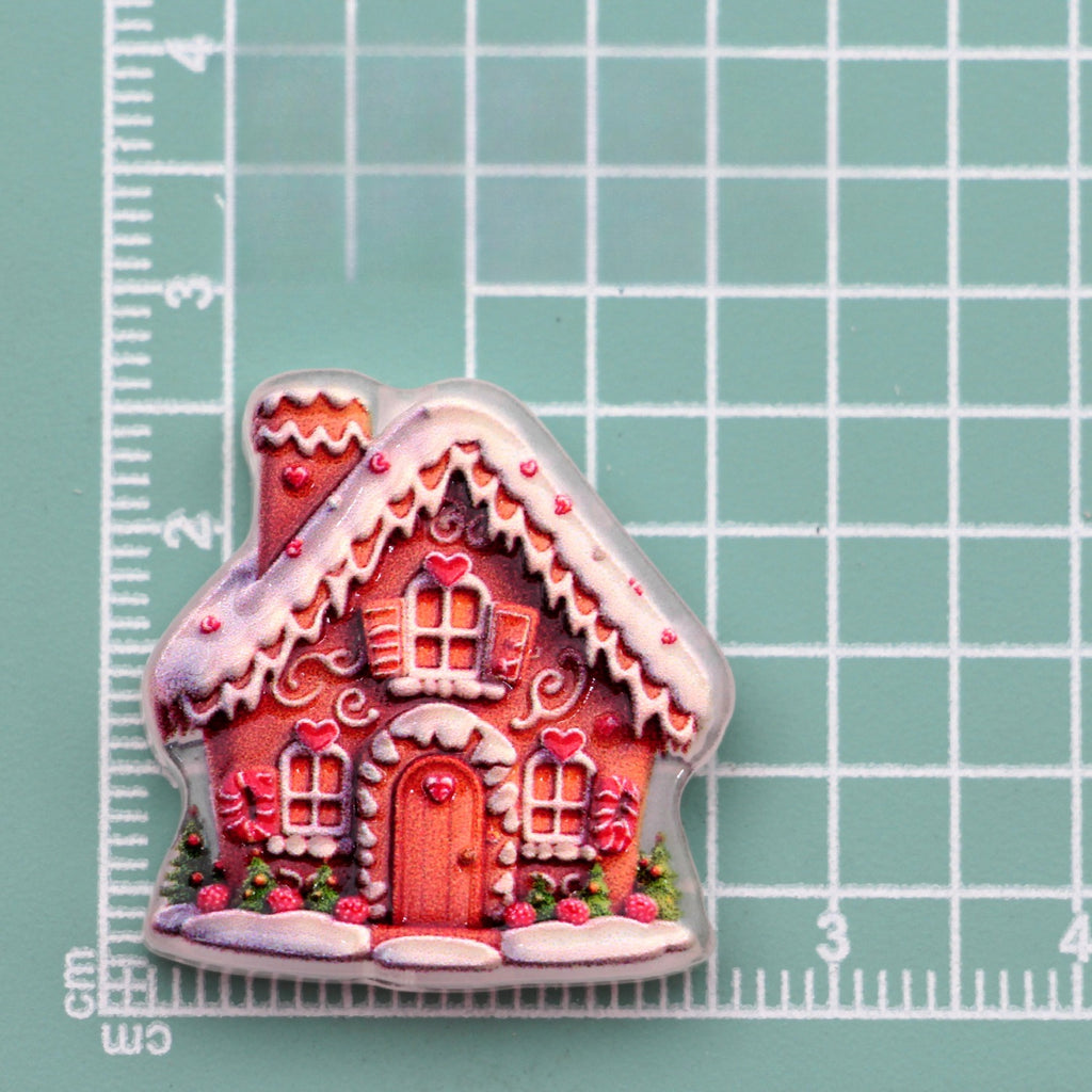 Gingerbread house acrylic charm with pink facade, white icing and red accents on green cutting mat