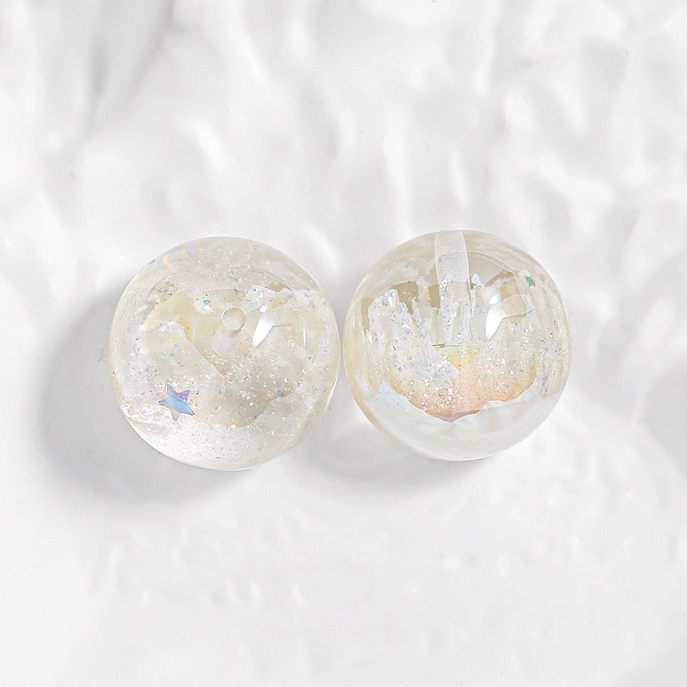 Two clear round resin beads filled with iridescent glitter and small star pieces on a white textured surface.