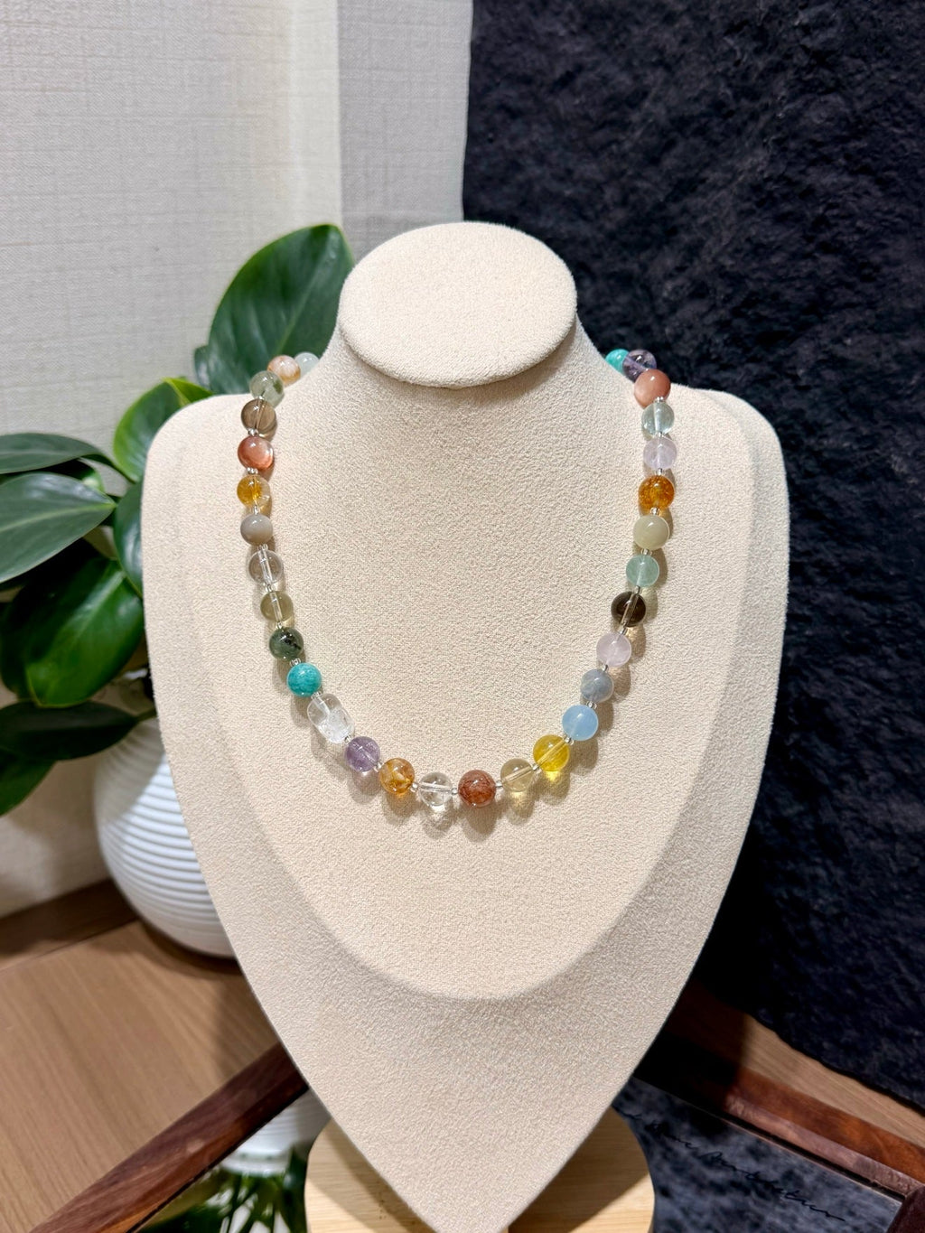 Multicolor faceted gemstone bead necklace on cream jewelry bust, turquoise yellow orange green purple stones