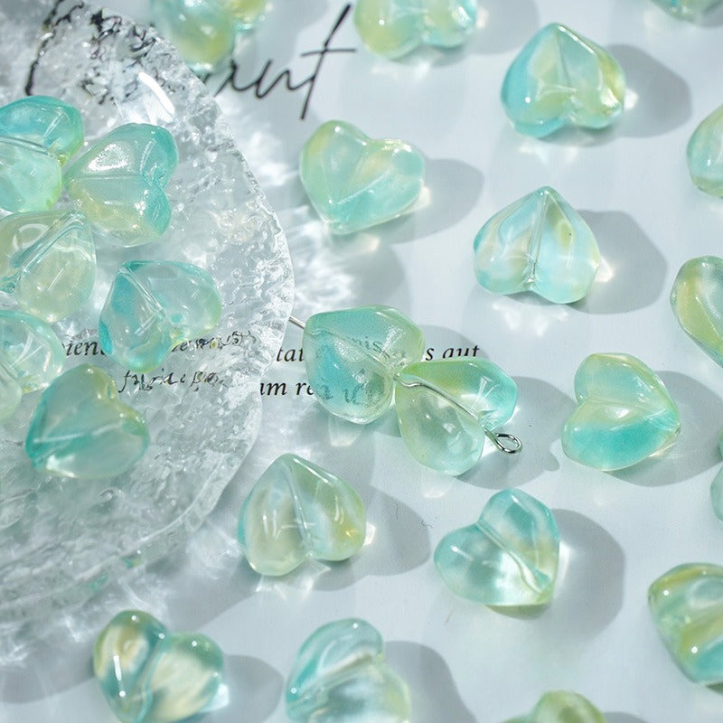 Heart-shaped translucent aqua green glass beads scattered on a white surface