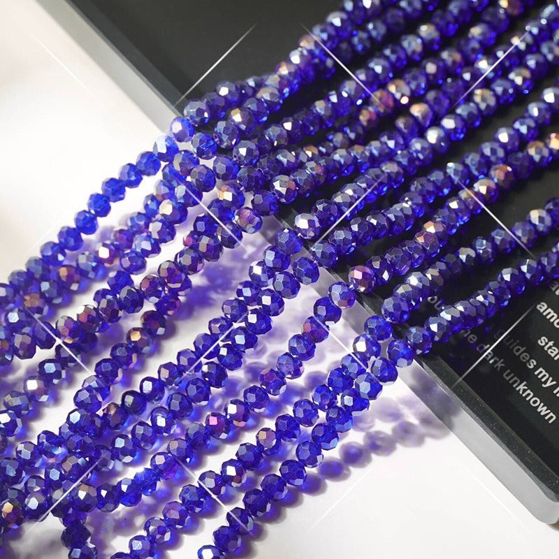 Multiple strands of faceted vivid cobalt blue crystal glass wheel beads arranged diagonally on white surface