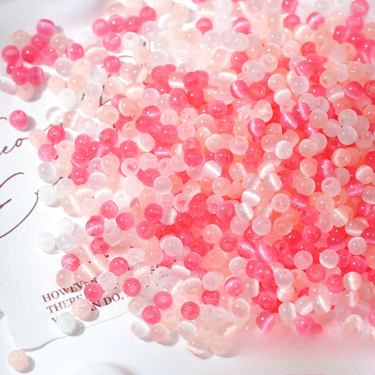 Close-up pile of frosted rose-pink cat's-eye glass beads on white surface