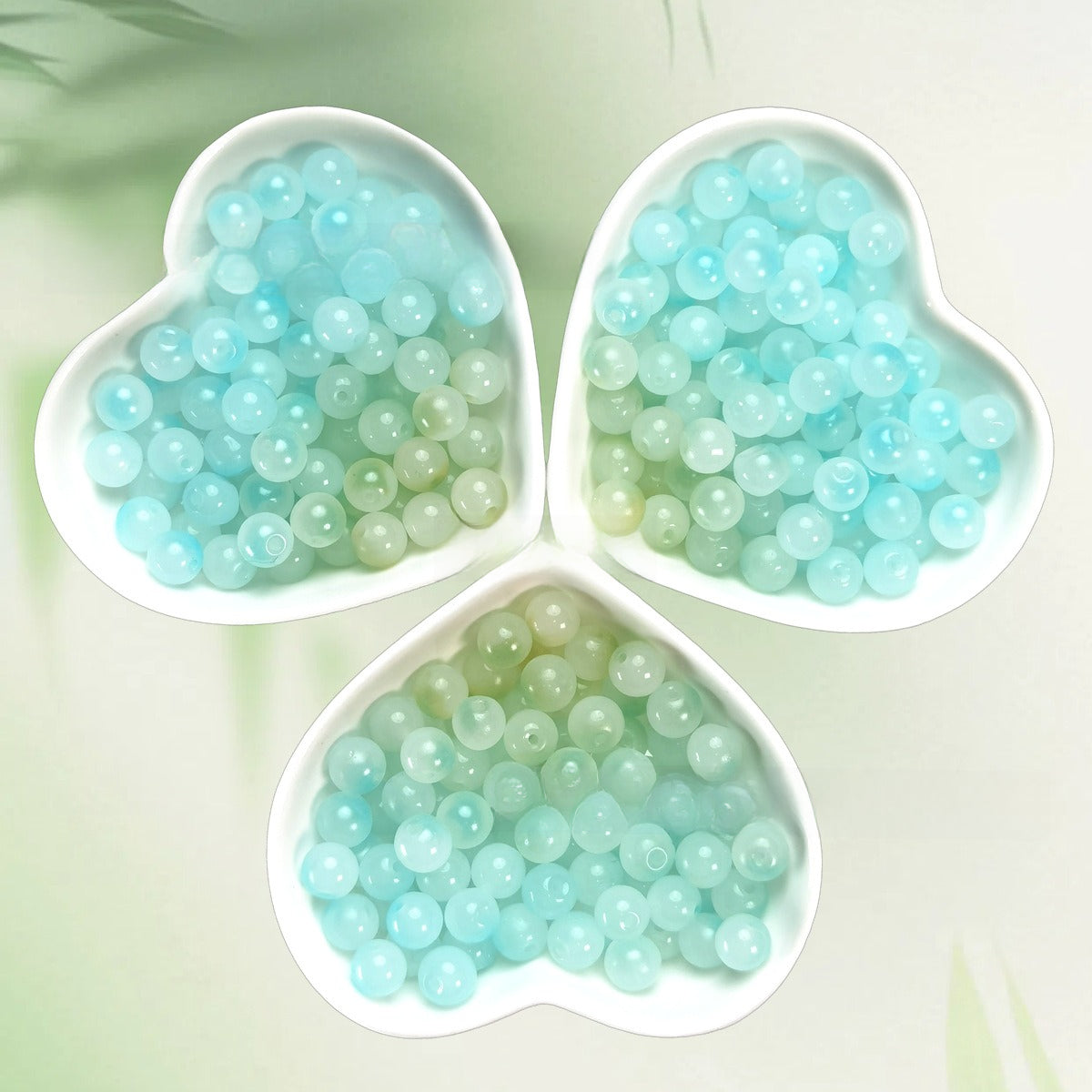 Three heart-shaped bowls of pale aqua and mint translucent beads on light green